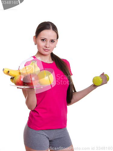 Image of Beautiful athlete holding a plate of fruit and dumbbell