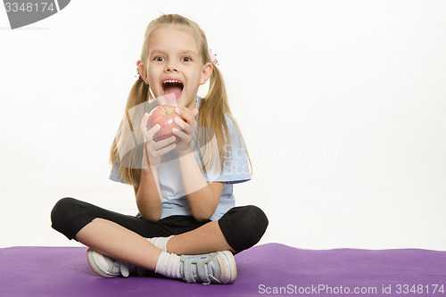 Image of Cheerful girl athlete eating apple