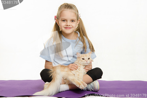 Image of Cheerful girl sitting a rug and stroked the cat on her lap