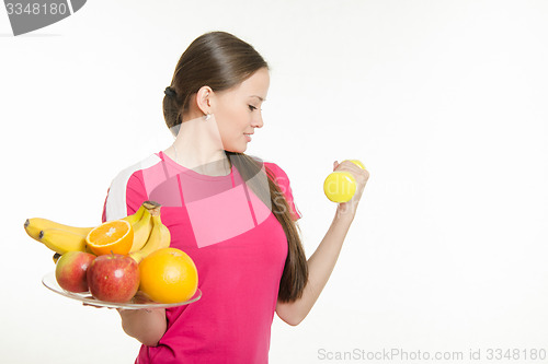 Image of Girl athlete dumbbell raises his hand and other holding a fruit