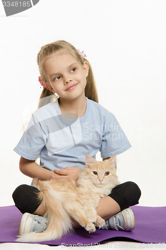 Image of Thoughtful girl with a cat on her lap sitting the mat