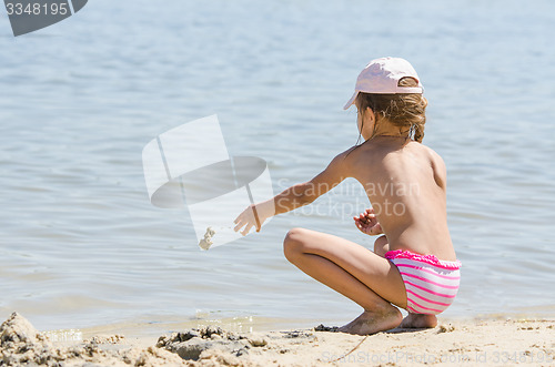 Image of Girl on the river throws sand in water