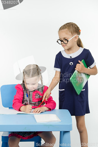 Image of The student writes in notebook under the supervision of a teacher