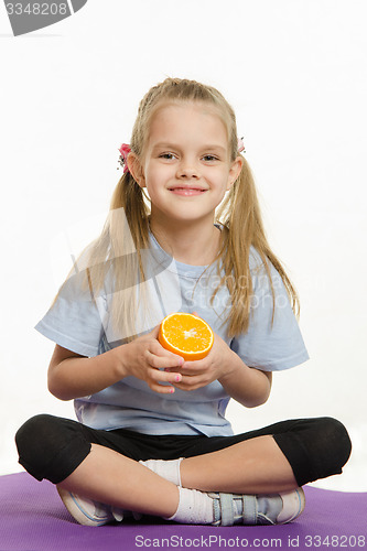 Image of Cheerful girl sitting with orange on the sports rug