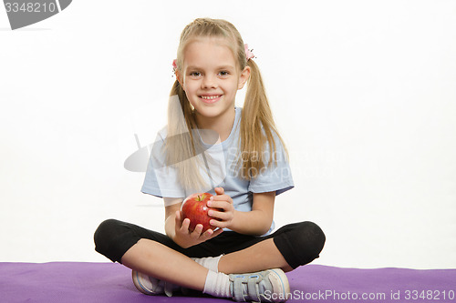 Image of Six year old girl sitting on a rug with an apple hands