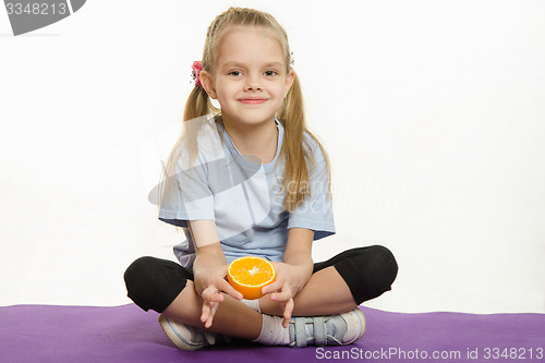 Image of Six year old girl sitting with orange on sport mat