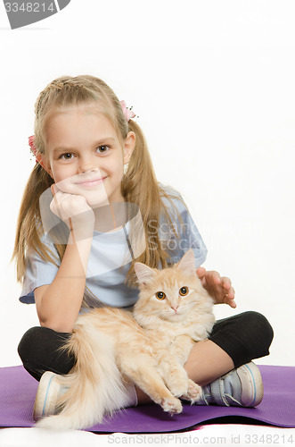 Image of Six year old girl athlete sitting on a rug with cat on her lap