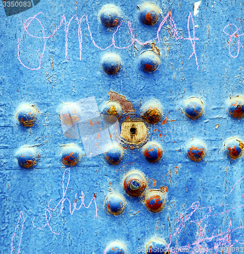 Image of dirty stripped paint in the blue wood door and rusty nail