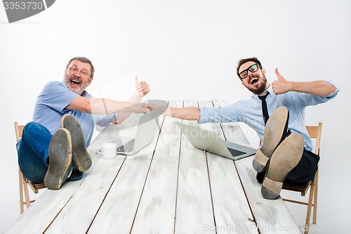 Image of The two smiling businessmen with legs over table