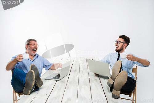 Image of The two businessmen with legs over table working on laptops
