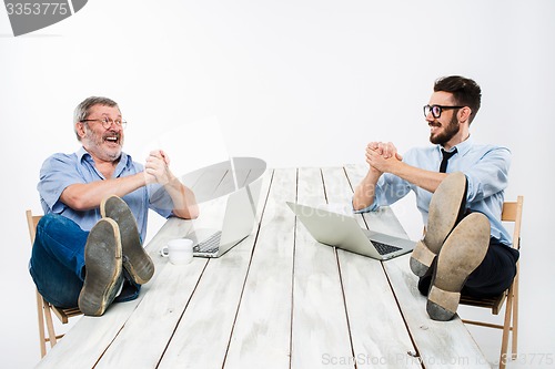Image of The two businessmen with legs over table working on laptops