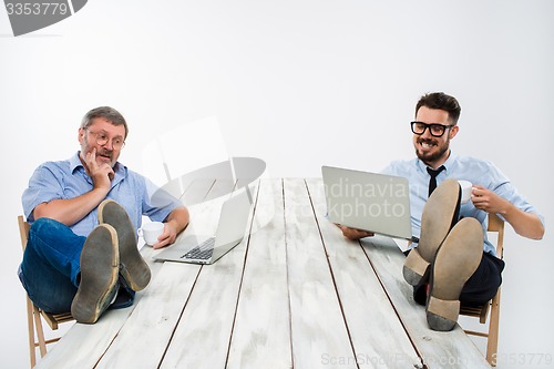 Image of The two businessmen with legs over table working on laptops