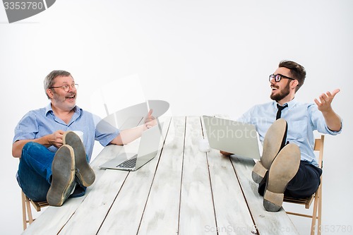 Image of The two businessmen with legs over table working on laptops