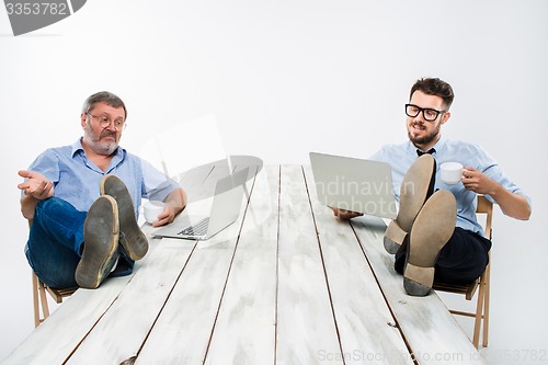 Image of The two businessmen with legs over table working on laptops