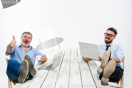 Image of The two businessmen with legs over table working on laptops