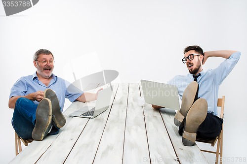 Image of The two businessmen with legs over table working on laptops