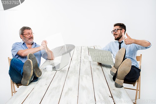 Image of The two businessmen with legs over table working on laptops