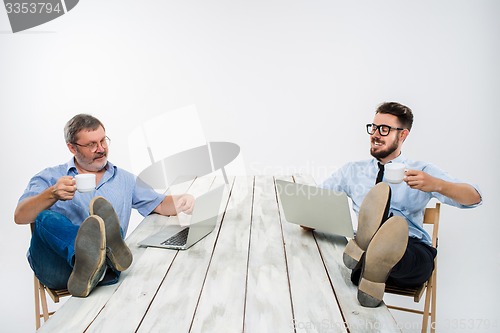 Image of The two businessmen with legs over table working on laptops