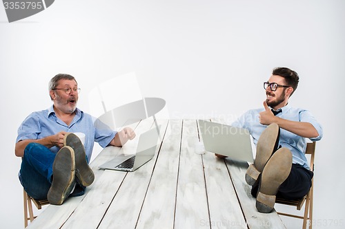 Image of The two businessmen with legs over table working on laptops