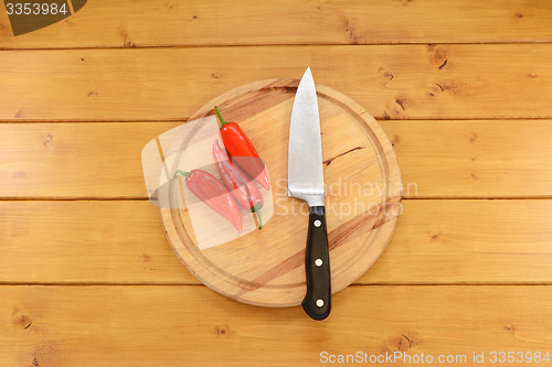 Image of Three red peppers with a knife on a chopping board 