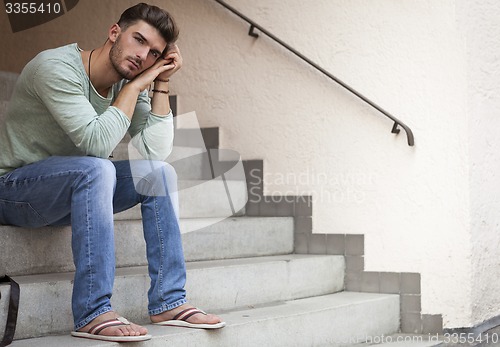 Image of Casual  young man sitting on steps