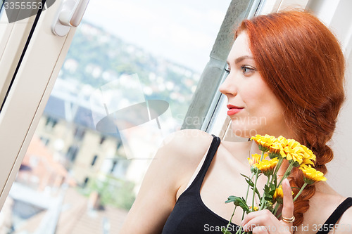 Image of Thoughtful Woman with Flowers Leaning on Window