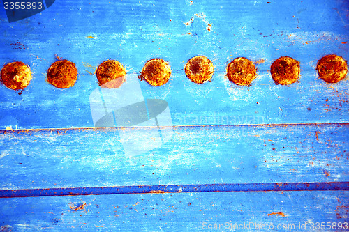Image of red  stripped paint in   blue wood door and rusty nail