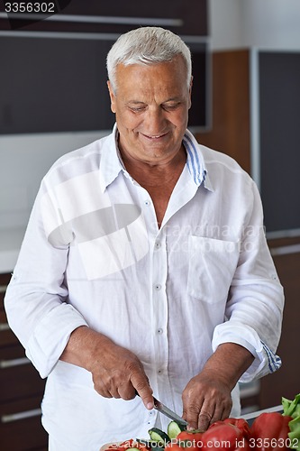 Image of senior man cooking at home preparing salad in kitchen