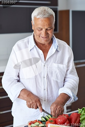 Image of senior man cooking at home preparing salad in kitchen