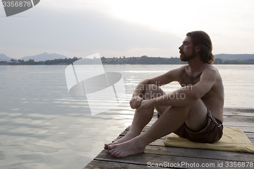 Image of Young man sitting at a bridge in evening light