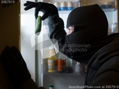 Image of Thief. Man in black mask with a cucumber.