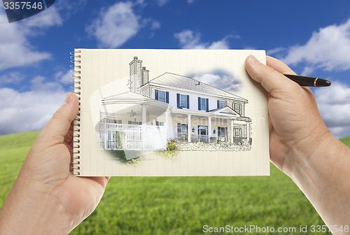 Image of Hands Holding Paper With House Drawing Over Empty Grass Field