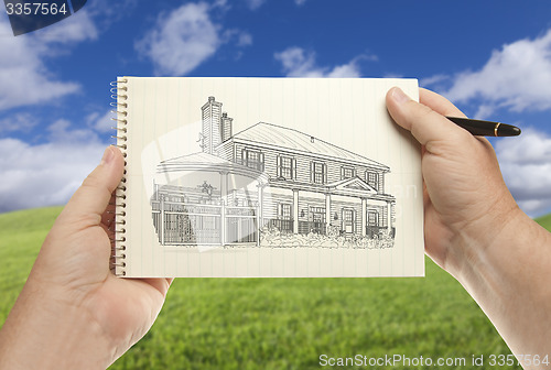 Image of Hands Holding Paper With House Drawing Over Empty Grass Field