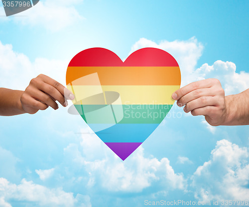 Image of human hands with rainbow heart shape over blue sky