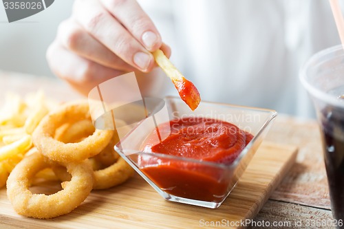 Image of close up of hand dipping french fries into ketchup