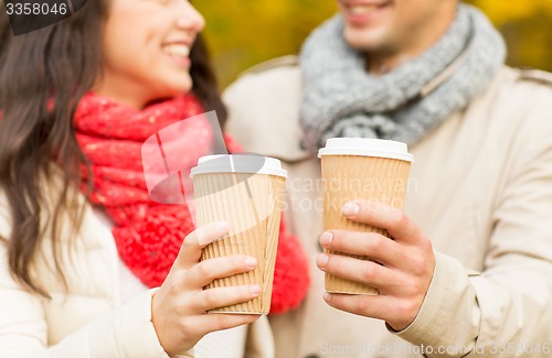 Image of smiling couple with coffee cups in autumn park