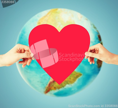 Image of human hands holding red heart over earth globe