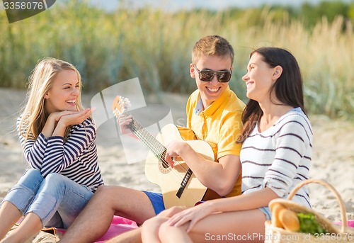Image of group of happy friends playing guitar on beach