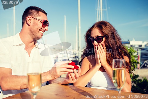 Image of smiling couple with champagne and gift at cafe