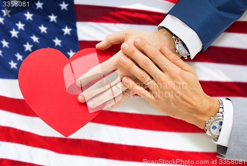 Image of close up of male gay couple hands with red heart