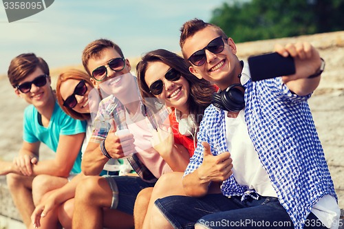 Image of group of smiling friends with smartphone outdoors