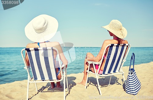 Image of happy women sunbathing in lounges on beach