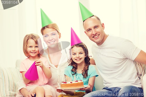 Image of smiling family with two kids in hats with cake