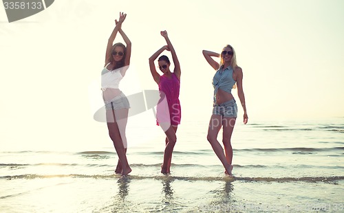 Image of happy female friends dancing on beach