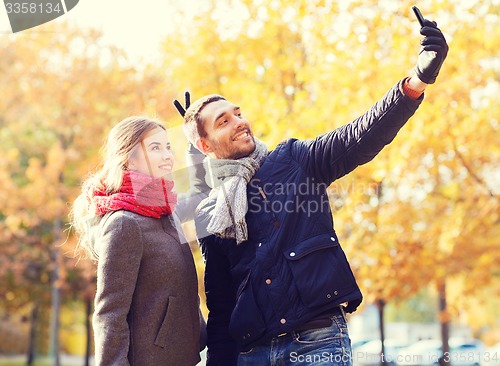 Image of smiling couple with smartphone in autumn park