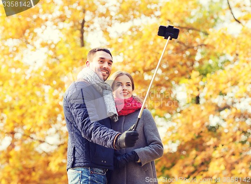 Image of smiling couple with smartphone in autumn park