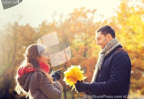 Image of smiling couple with bunch of leaves in autumn park