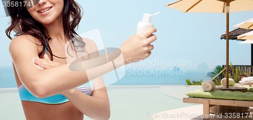 Image of happy young woman in swimsuit applying sunscreen