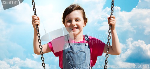 Image of happy little girl swinging on swing over blue sky