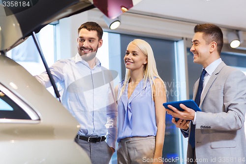 Image of happy couple with car dealer in auto show or salon